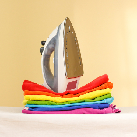 Iron stands with stacks of ironed colored linen. Pile of clothes. Ironing concept. All colors of the rainbowの写真素材