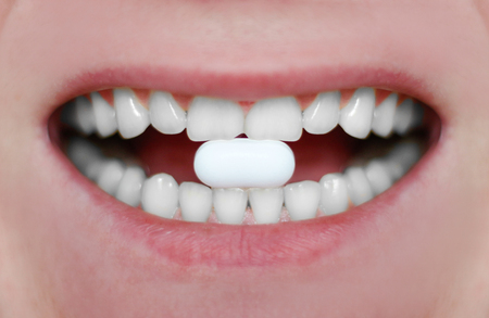 Close-up of a white pill in the male's mouth. Cushion gum on the teeth.の写真素材