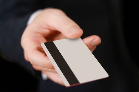 Businessmen holding credit card proposing it to you. Hand in black suit holds out a blank grey...