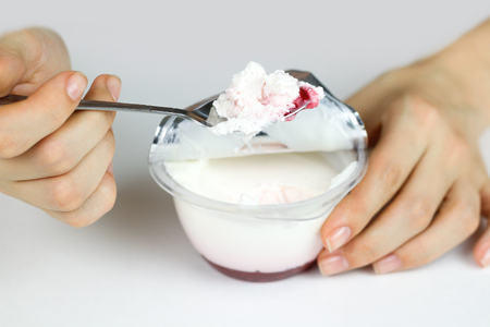 Girl's hand stirred with a spoon of natural yogurt and red jam. Yogurt on the spoon close up. Isolated on white background.の写真素材