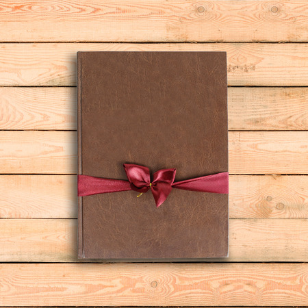 Brown book gift. With red ribbon and bow. On a wooden table.の写真素材