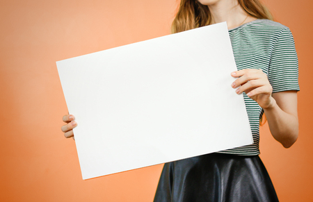 Woman showing blank white big A2 paper. Leaflet presentation. Pamphlet hold hands. Girl show clear offset paper. Sheet template. Booklet design sheet display read first personの写真素材