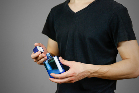 Man in black t shirt holding blue bottle toilet water. Close up, mock up. Isolated.の写真素材