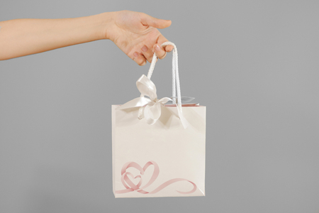 Blank white paper gift bag with hearts mock up holding in hand. Empty plastic package mockup hold in hands isolated. Consumer pack ready for logo design or identity presentation. Product packet handleの写真素材
