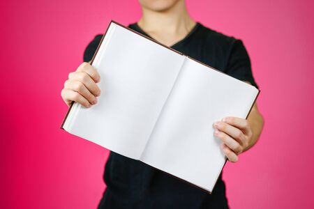 Closeup of guy in black t-shirt holding blank open white book on isolated background. Education concept. Mock up.の写真素材