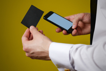 Businessman holding mobile phone and a business card (visit card) with text contact us. Close up. Isolated backgroundの写真素材
