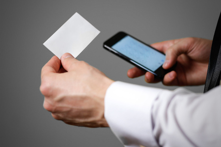 Businessman holding mobile phone and a business card (visit card) with text contact us. Close up....