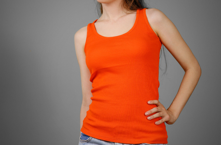 A girl in a orange plain t-shirt. Empty tank top. Closeup. Isolated on grey background.の写真素材