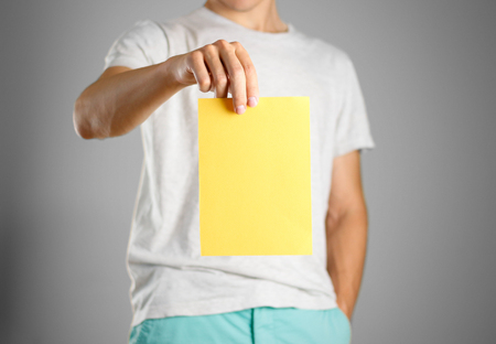 A man in a gray t-shirt holding blank clear yellow of the sheet. Closeup. Isolated.の写真素材