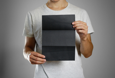 A man in a gray t-shirt holding blank clear black of the sheet. Closeup. Isolated.の写真素材