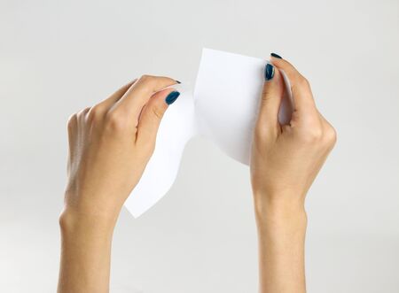 Female hands rip a white sheet of paper. Isolated on gray background. Closeup.