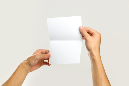 Male hands holding a white sheet of paper. Isolated on gray background. Closeup.