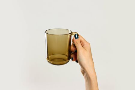 Female hand holding black empty glass mug. Isolated on gray background. Closeup.の写真素材