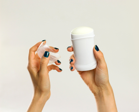 Female hands holding white deodorant. Isolated on gray background. Closeup.