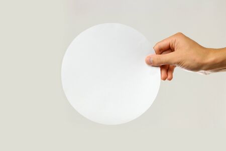 Male hands holding a white sheet rounded of paper. Isolated on gray background. Closeup.