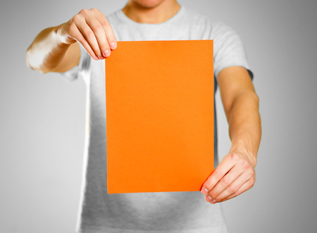A man in a gray t-shirt keeps a orange clean blank sheet of A4. Isolated on grey background.の写真素材