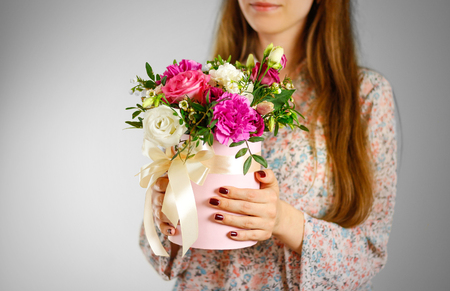 Girl holding in hand rich gift bouquet. Composition of flowers in a pink hatbox. Tied with wide white ribbon and bow.の写真素材