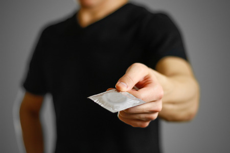 Man's hand holding a single condom. Close up. Isolated on grey background.の写真素材
