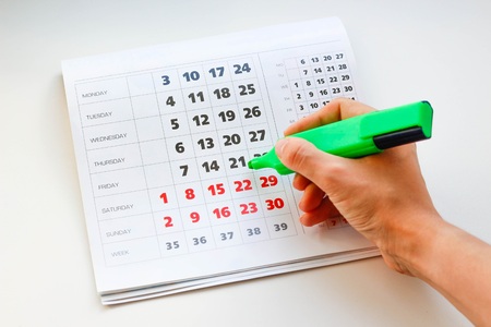 Hand crosses off the green marker days in the calendar. White calendar. Weekends are highlighted in red. Close upの写真素材