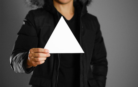 A man in a warm winter jacket holds a triangular white leaflet. Blank paper. Close up. Isolated...