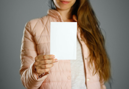 A woman in a warm winter jacket holding a white leaflet. Blank paper. Close up. Isolated background.