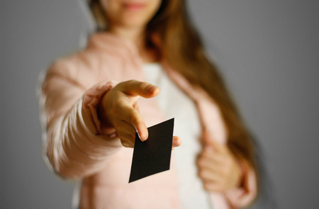 A woman in a warm winter jacket holding a black leaflet. Blank paper. Close up. Isolated background.の写真素材