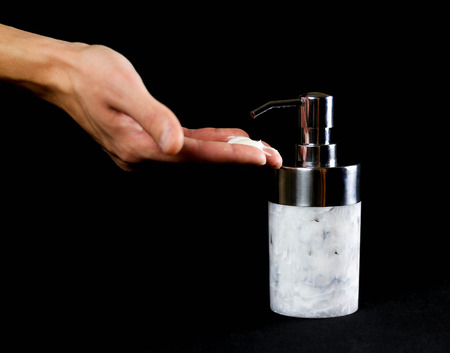 Hand presses on a beautiful bottle of liquid soap. Close up. Isolated on black backgroundの写真素材