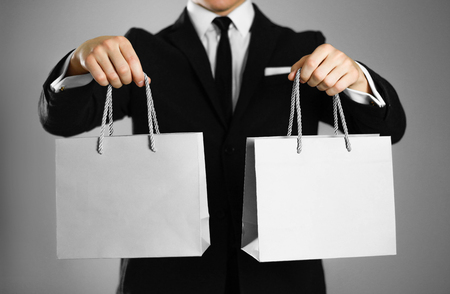 Businessman in a black suit holding a gray paper gift bag. Close up. Isolated background.の写真素材