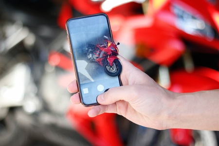 Hand taking pictures on the phone camera sports red motorcycle.