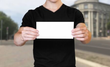 A man holding a white sheet of paper. Holding a booklet. Close up. The background of the city.の写真素材