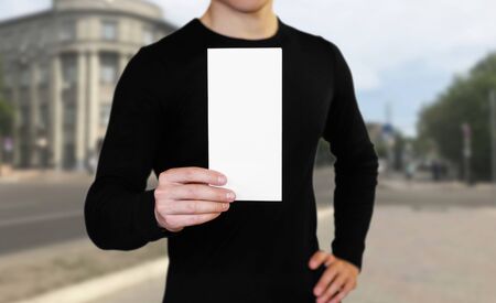 A man holding a white sheet of paper. Holding a booklet. Close up. The background of the city.の写真素材