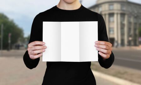 A man holding a white sheet of paper. Holding a booklet. Close up. The background of the city.の写真素材