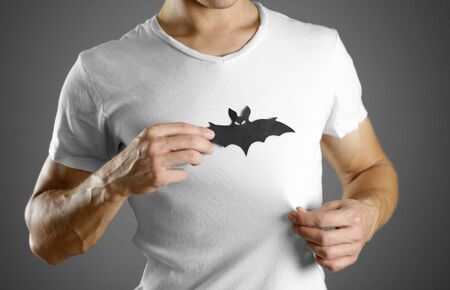 A man in a white t-shirt holds a black silhouette of a bat. Close up.の写真素材