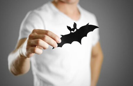 A man in a white t-shirt holds a black silhouette of a bat. Close up.の写真素材