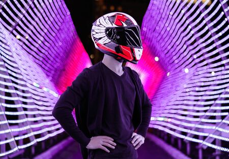 A motorcyclist in helmet stands among many lanterns. A lot of light effects. Middle of the light street. Night city.の写真素材