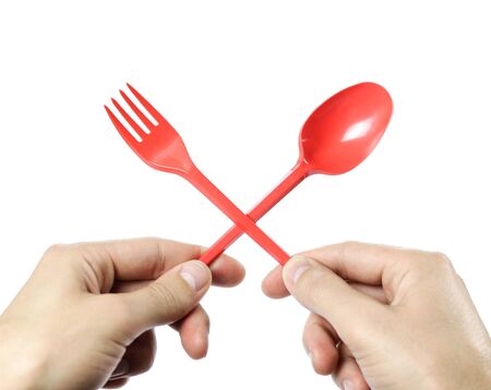 Hands holding plastic red disposable spoon and fork crossed. Close up. Isolated on white background.の写真素材