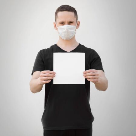 A man in a medical mask holds a blank white sheet of paper. Close up. Isolated on a grey background.の写真素材