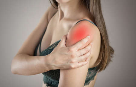 Shoulder pain in a woman. Highlighted in red. On a gray background. Close up.の写真素材