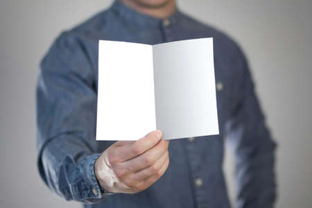 A man holds a white piece of paper. A flyer in the hands of a man. Prepared for your text. Isolated on a gray background.の写真素材