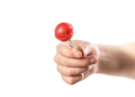 The hand holds a red lollipop on a stick. Close up. Isolated on a white background.の写真素材