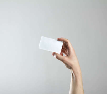 The hand holds an empty white business card. A clean flyer in your hands. For your text. Isolated on a gray backgroundの写真素材