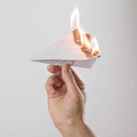 A hand holds a burning paper airplane. Close up. Isolated on a gray background.の写真素材