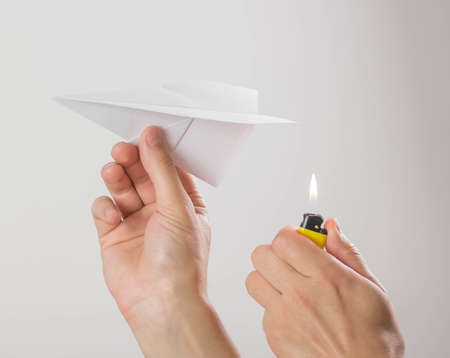 A hand holds a burning paper airplane. Close up. Isolated on a gray background.の写真素材