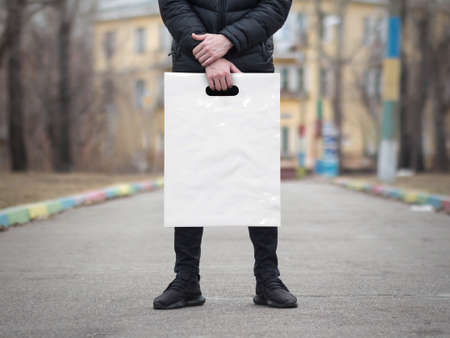 A man holds a mockup white plastic bag. A man with a package on the street in the park.の写真素材