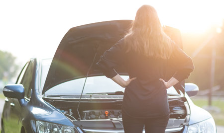 The girl is standing near the open hood of the car. The car needs repair.