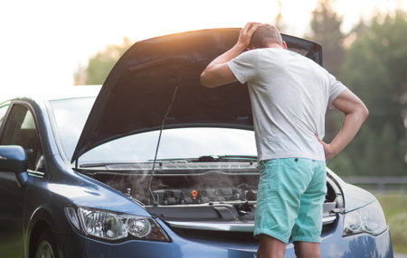 A man stands near the open hood of a car. The car needs repair.の写真素材