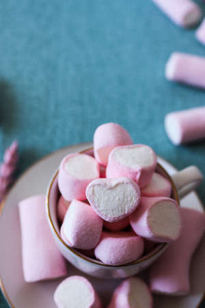 Sweet pink marshmallows on blue background. A marshmallow is shaped like a heart. Along with dried pink flowers. Female image, adorable and with an ideal shape for stories and square post.の写真素材
