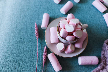 Sweet pink marshmallows on blue background. A marshmallow is shaped like a heart. Along with dried pink flowers. Female image, adorable and with an ideal shape for stories and square post.の写真素材