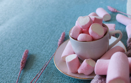 Sweet pink marshmallows on blue background. A marshmallow is shaped like a heart. Along with dried pink flowers. Female image, adorable and with an ideal shape for stories and square post.の写真素材
