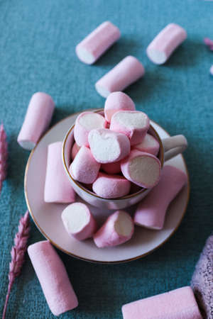 Sweet pink marshmallows on blue background. A marshmallow is shaped like a heart. Along with dried pink flowers. Female image, adorable and with an ideal shape for stories and square post.の写真素材